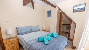 A bedroom with a bed, wooden nightstands, a dresser, a radiator, and a painting on the wall. - Seamark - Two Bedroom Apartment, Sleeps 4 (Woolacombe)