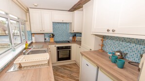 A compact kitchen with white cabinets, a wooden countertop, a built-in oven, and a small refrigerator. - Seamark - Two Bedroom Apartment, Sleeps 4 (Woolacombe)