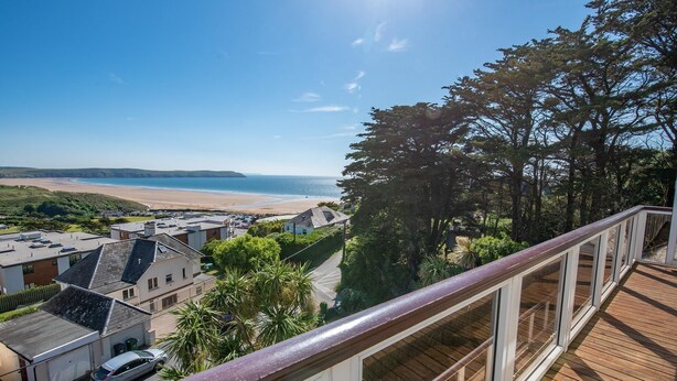 A coastal view from a balcony with a wooden deck, overlooking a beach and a town. - Seamark - Two Bedroom Apartment, Sleeps 4 (Woolacombe)