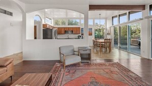 A spacious living area with a large rug, a sofa, and a dining table with chairs. There is a kitchen area visible through an archway, and a balcony with a railing. - Uptown Home w/ Amazing Views and Hot Tub (Sedona)