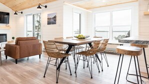 A spacious dining area with a large wooden table surrounded by wicker chairs, a brown sofa, and a small round table with a bowl of fruit.