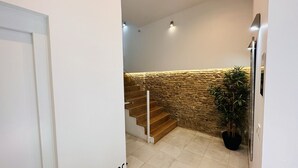 A staircase with wooden steps and a textured stone wall, leading to a landing area with a potted plant. - Apto Plus 1 Dorm. Int. 1ª Planta (Cádiz)