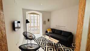 A modern living room with a sofa, two chairs, a patterned rug, and a wall-mounted TV. - Apto Plus 1 Dorm. Int. 1ª Planta (Cádiz)