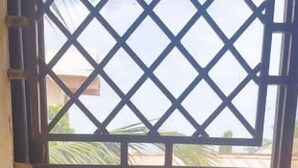 Una cocina con un lavamanos de acero inoxidable, una ventana con celosía metálica y un salpicadero de azulejos blancos.