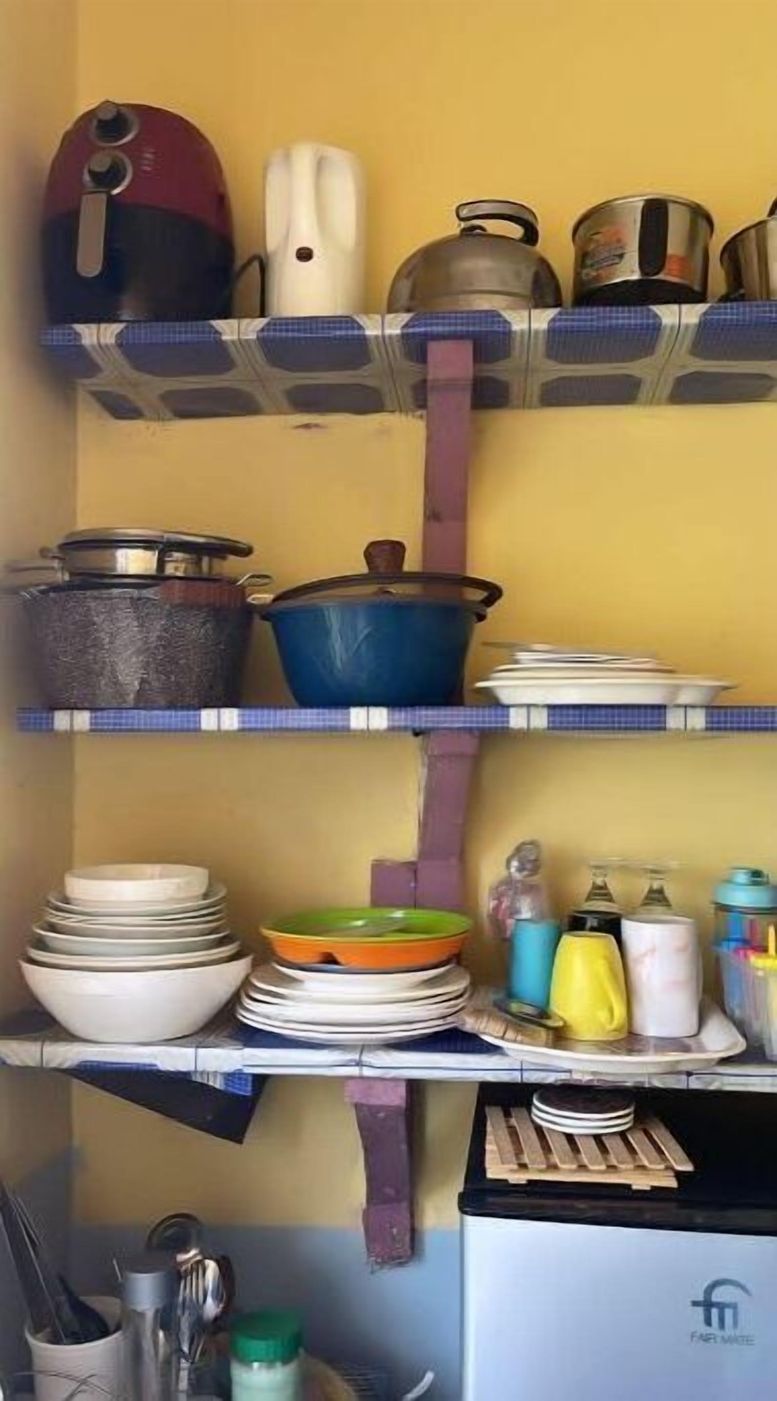 A kitchen with shelves holding various kitchenware, including pots, pans, and plates.