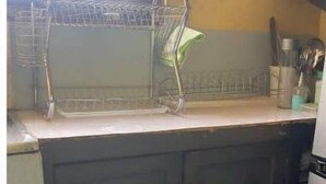 Una cocina con armarios oscuros, un escurreplatos y una ventana con mosquitero.