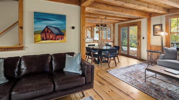 Una sala de estar acogedora con un sofá de cuero, un comedor con mesa y sillas de madera, y un ventanal con vistas al exterior.