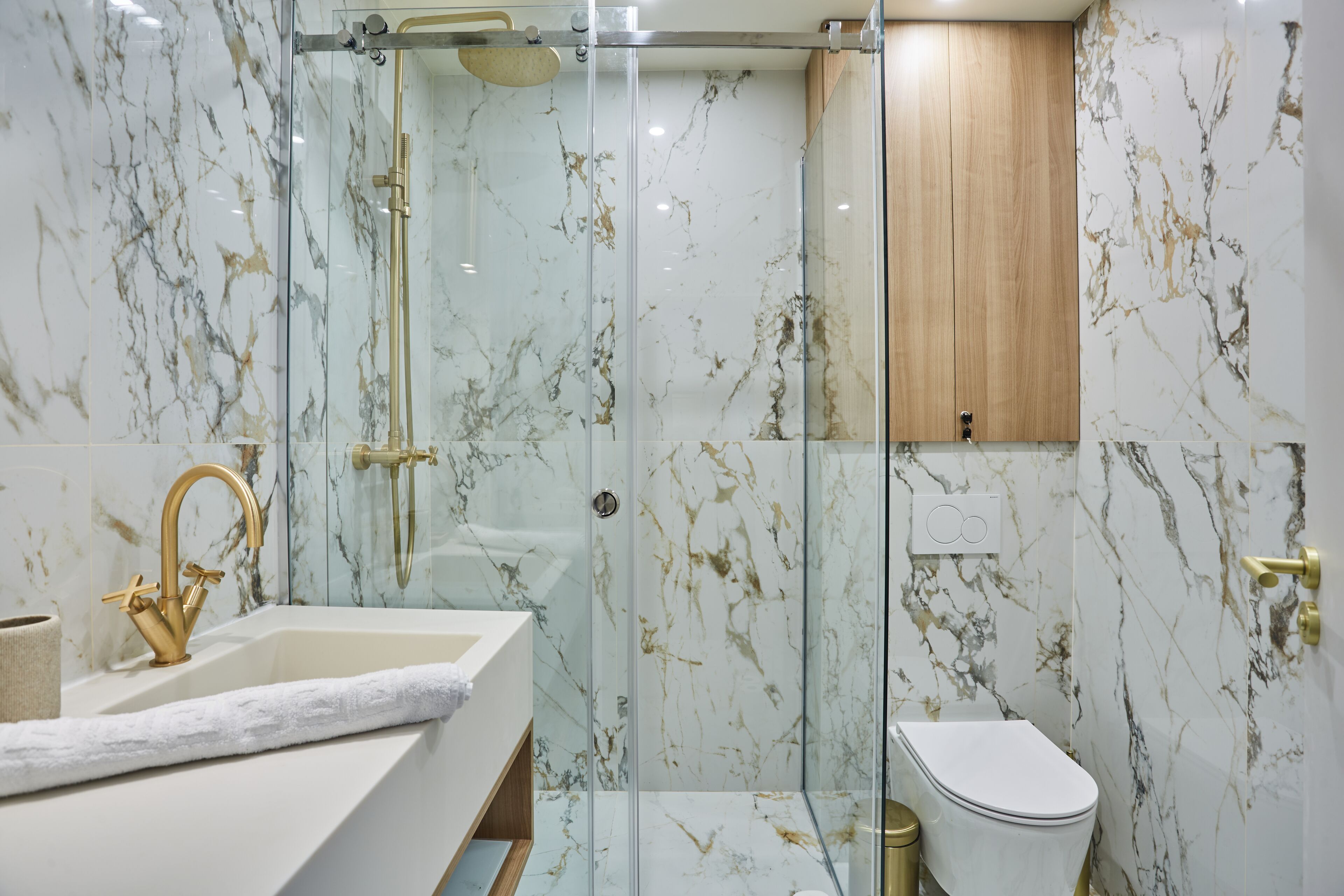 A modern bathroom with a glass-enclosed shower, a gold faucet, and a marble backsplash.