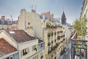 A narrow street lined with multi-story buildings, featuring balconies with plants and a prominent church steeple in the background. - Apart Hotel Centre de Paris by Studio prestige (Paris)