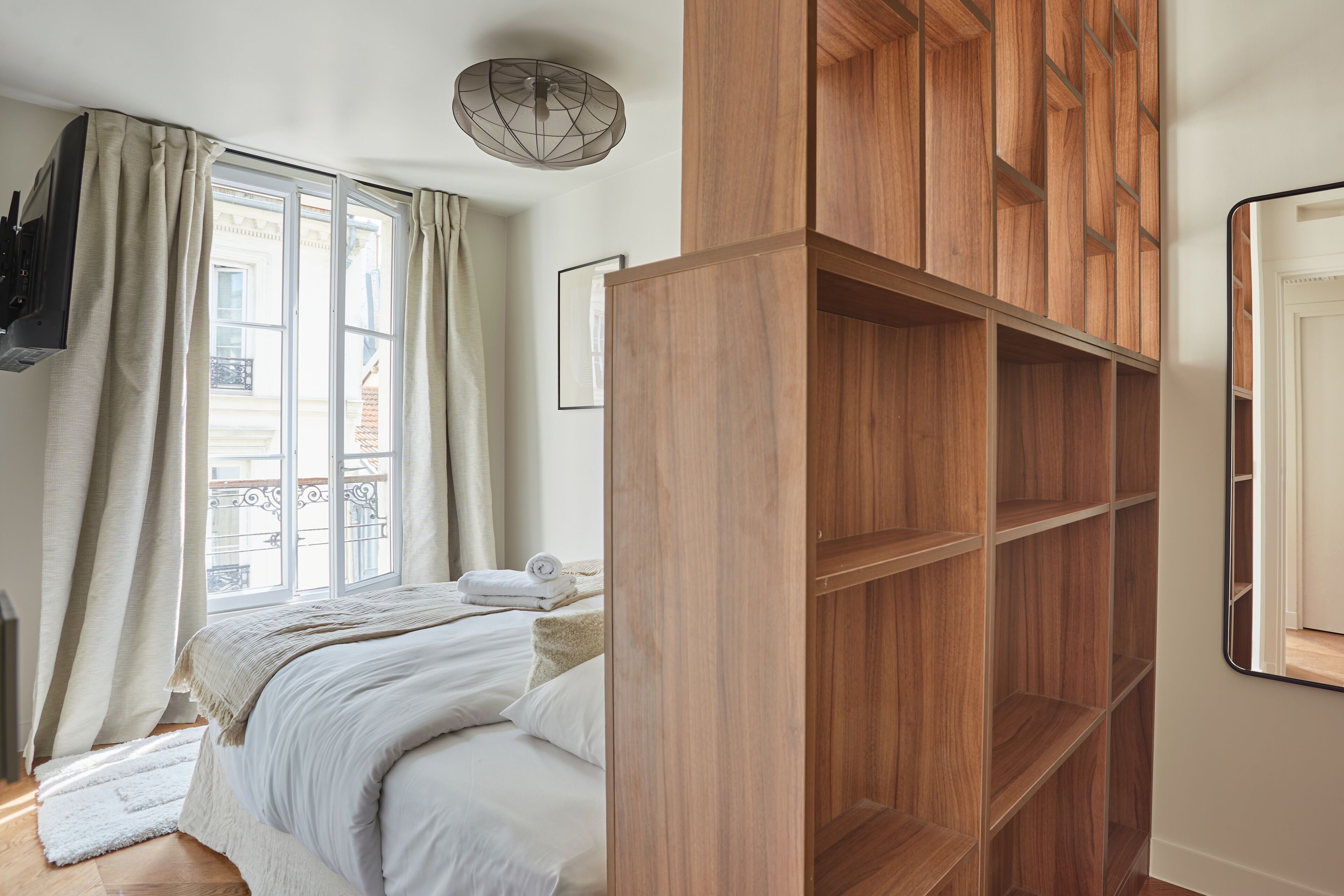 A bedroom with a large bed, a wooden wardrobe, and a window with curtains.