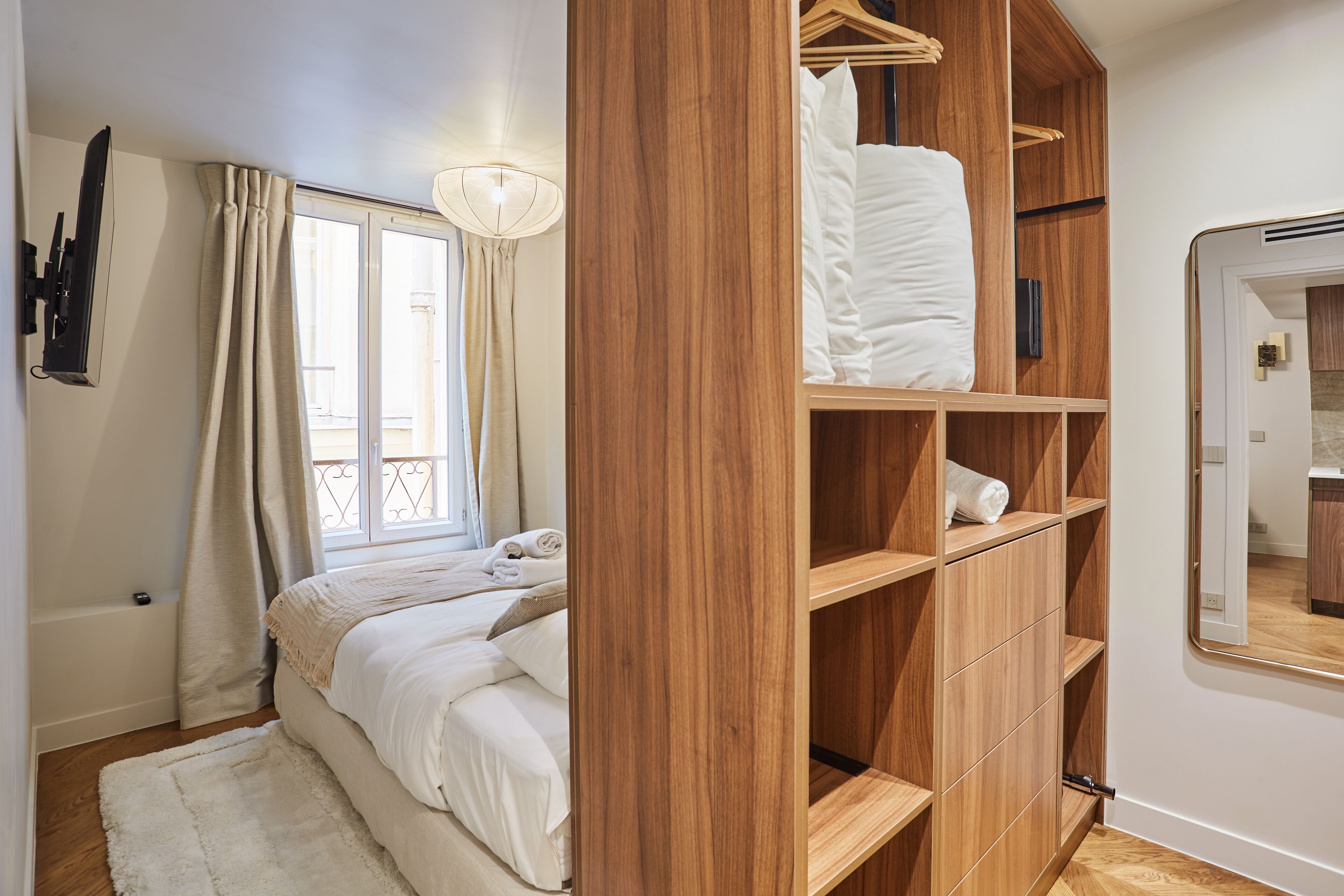 A bedroom with a bed, wooden wardrobe, and a bathroom mirror.