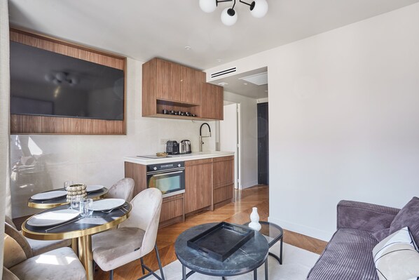 A modern kitchen with wooden cabinets, a built-in oven, and a dining area with a round table and chairs. - Apart Hotel Centre de Paris by Studio prestige (Paris)