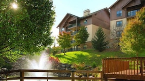Ein mehrstöckiges Gebäude mit Balkonen, einem Teich mit Springbrunnen und einer Holzterrasse.