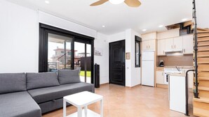 Um apartamento moderno com um sofá cinzento, uma mesa de centro branca, uma cozinha com armários de madeira e uma porta preta.