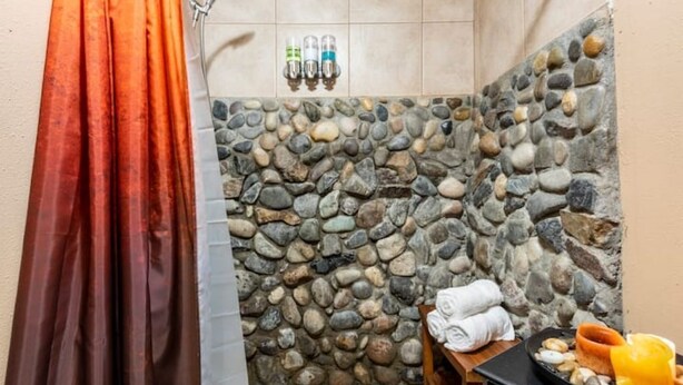 Un petit espace douche aux murs en pierre, équipé d’un rideau, d’un porte-serviettes et d’un plateau contenant des articles de toilette.