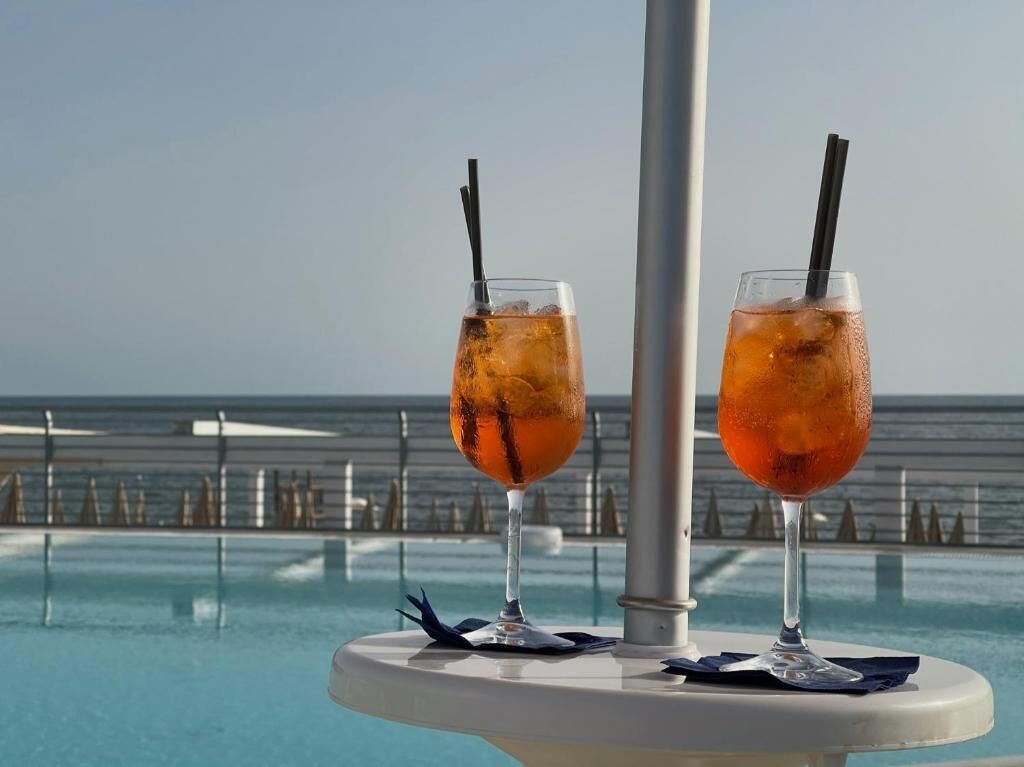 Two cocktails on a table by a pool with a view of the ocean.