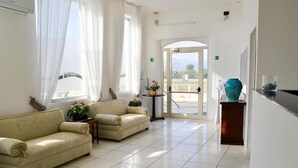 A spacious lobby with two sofas, a small table with a vase, and a large window with curtains. - Blu Hotel  (Pontecagnano Faiano)