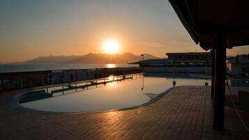 Una piscina con vista sul tramonto, una zona riparata e un edificio sullo sfondo.