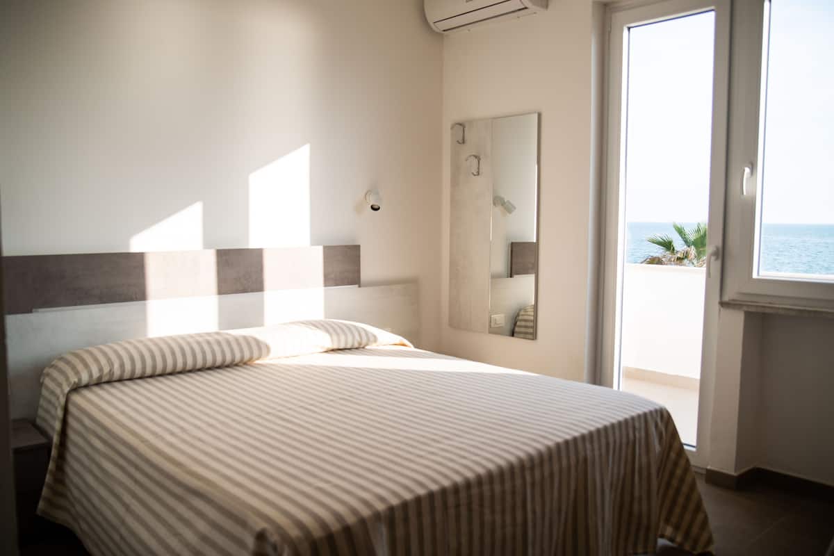 A hotel room with a bed, a large window, and a view of the sea.