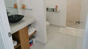 Kylpyhuoneessa on musta pesuallas, valkoinen wc-istuin ja lasihyllyt, joilla on hygieniatuotteita.