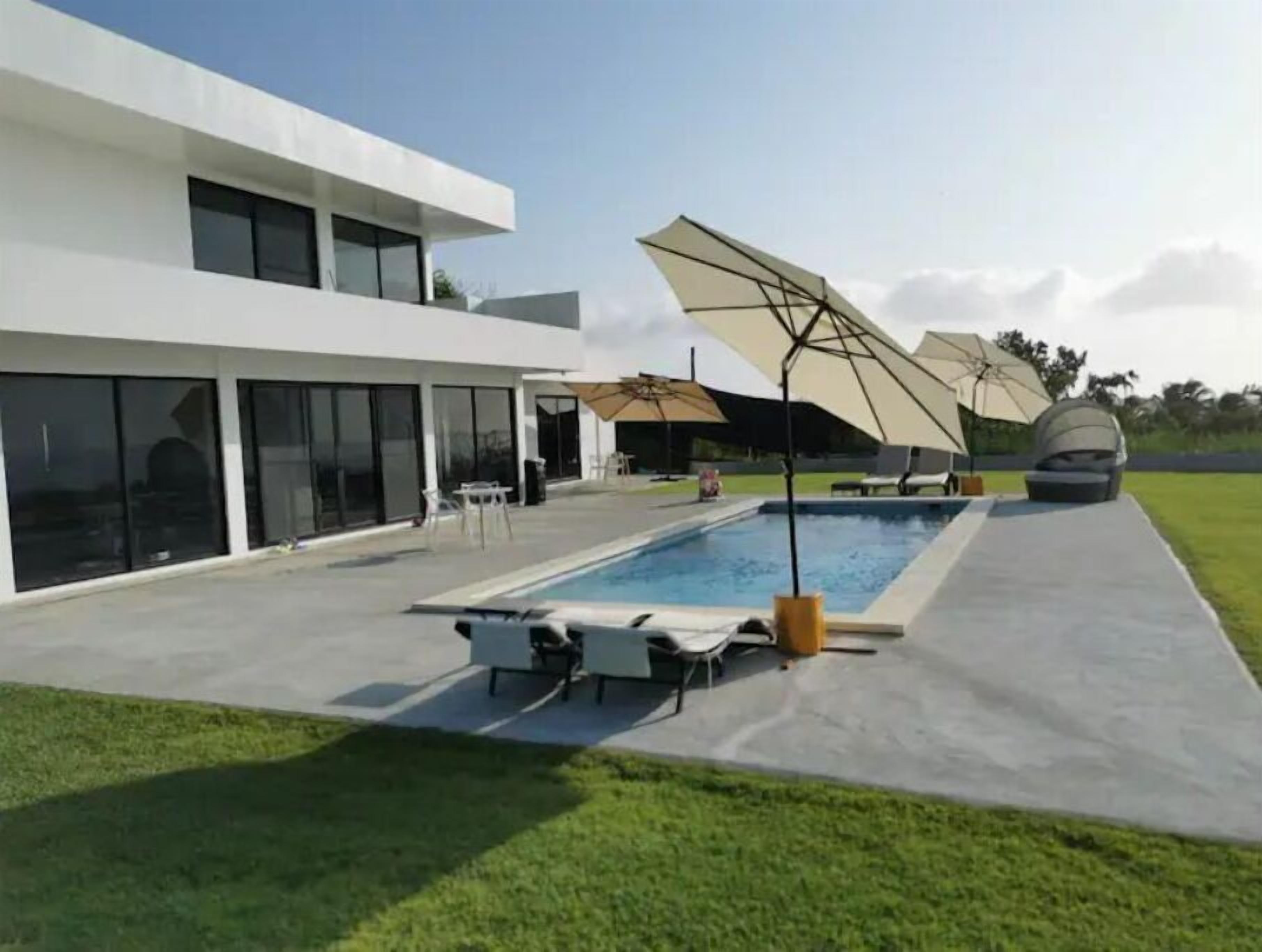 A modern house with a swimming pool, outdoor furniture, and umbrellas.