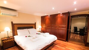 Una habitación de hotel con una cama grande, cabecera de madera, dos mesitas de noche con lámparas, un armario de madera y suelo de baldosas.