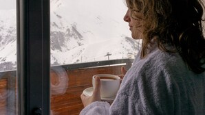 A person in a robe holding a cup, looking out of a window at a snowy mountain landscape. - Gudauri Ski Resort - Twins Apartments (Kazbegi)