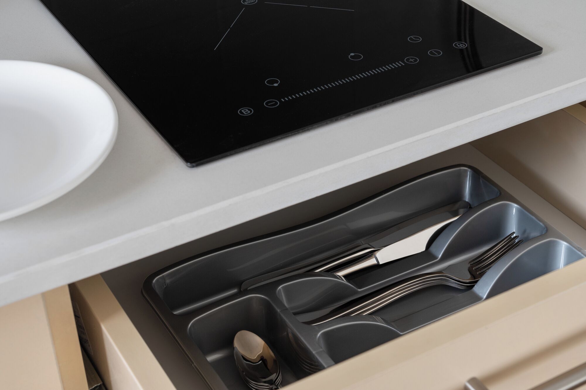 A kitchen with a black induction cooktop, a white bowl, and a drawer organizer with utensils.