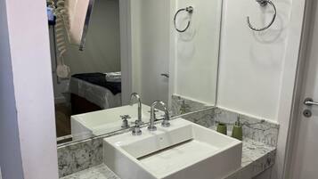 A modern bathroom with a double sink, a large mirror, and a shower area visible in the background.