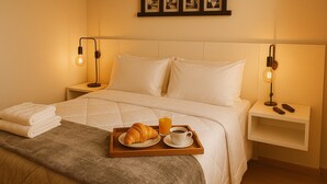 A neatly made bed with a tray of croissant, coffee, and juice, and bedside lamps. - Elegance Suites Alvorada (São Paulo)