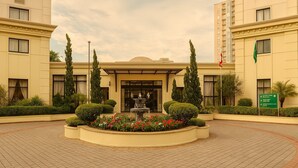 A hotel entrance with a central fountain, surrounded by well-manicured hedges and flower beds. - Elegance Suites Alvorada (São Paulo)