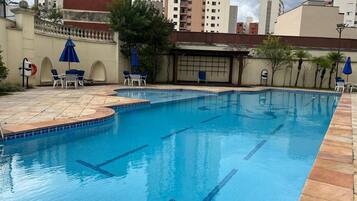 A swimming pool with tiled edges and a tiled deck area, surrounded by lounge chairs and umbrellas.