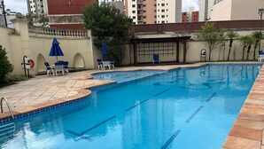 A swimming pool with a tiled deck, lounge chairs, and umbrellas. - Elegance Suites Alvorada (São Paulo)