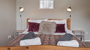 A neatly made bed with a patterned bedspread, two bedside tables, a window with blinds, and two wall-mounted lamps.