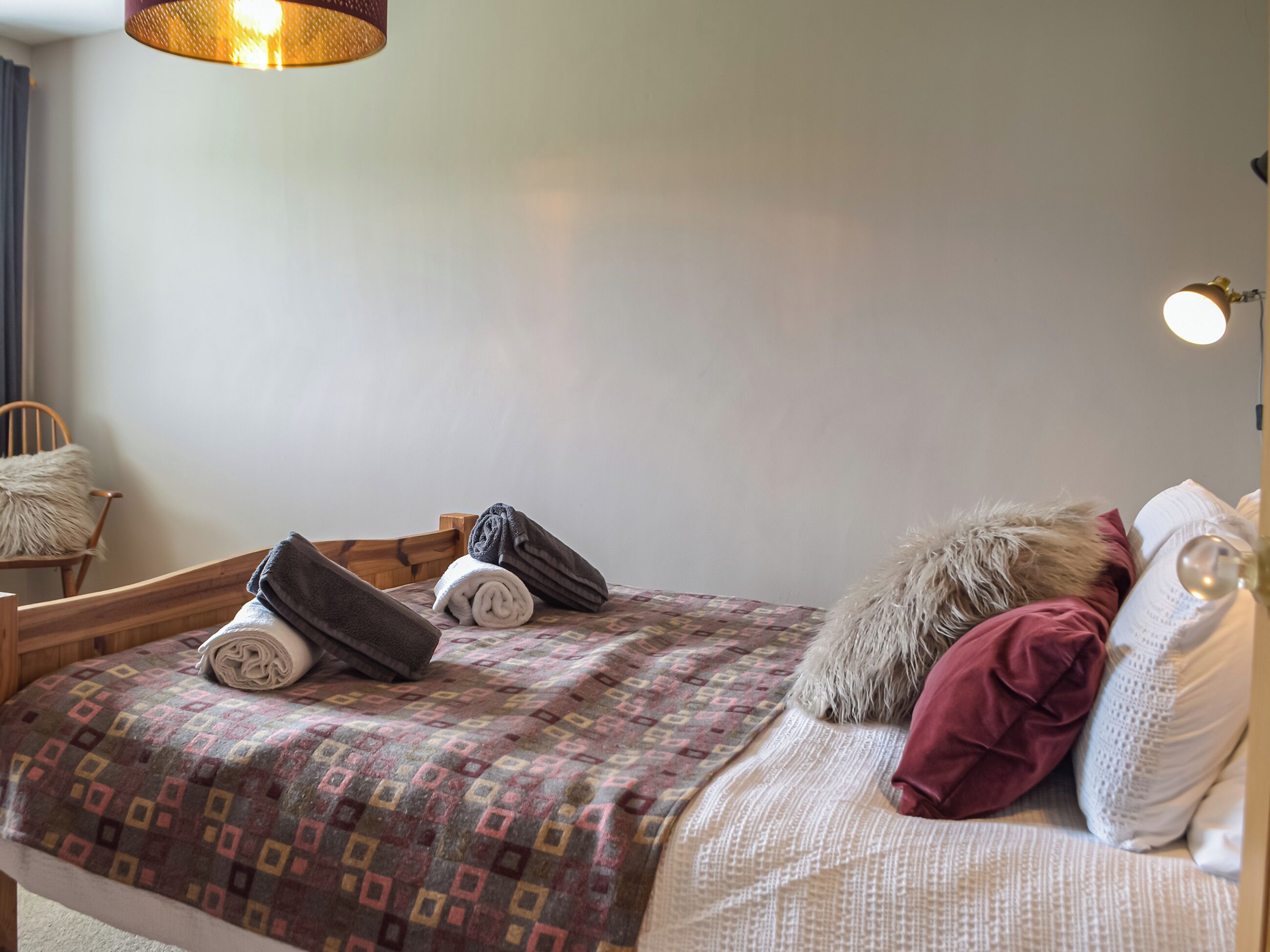 A neatly made bed with a patterned blanket, a fluffy pillow, and rolled towels.