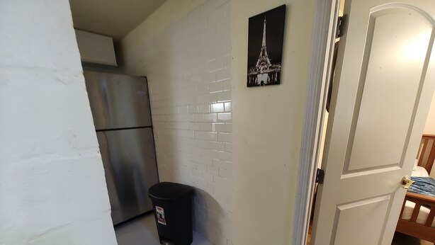 A kitchen with a stainless steel refrigerator, a black trash bin, and a tiled wall with a picture of the Eiffel Tower. - 2 bedroom one bath  holiday FL
 (Holiday)