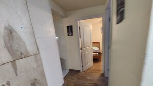 A narrow hallway with a tiled wall on one side and a wooden floor. A door leads to a bedroom with a bed and a nightstand. - 2 bedroom one bath  holiday FL
 (Holiday)