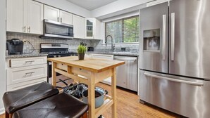 A modern kitchen with white cabinets, stainless steel appliances, a wooden table, and a black leather bench.