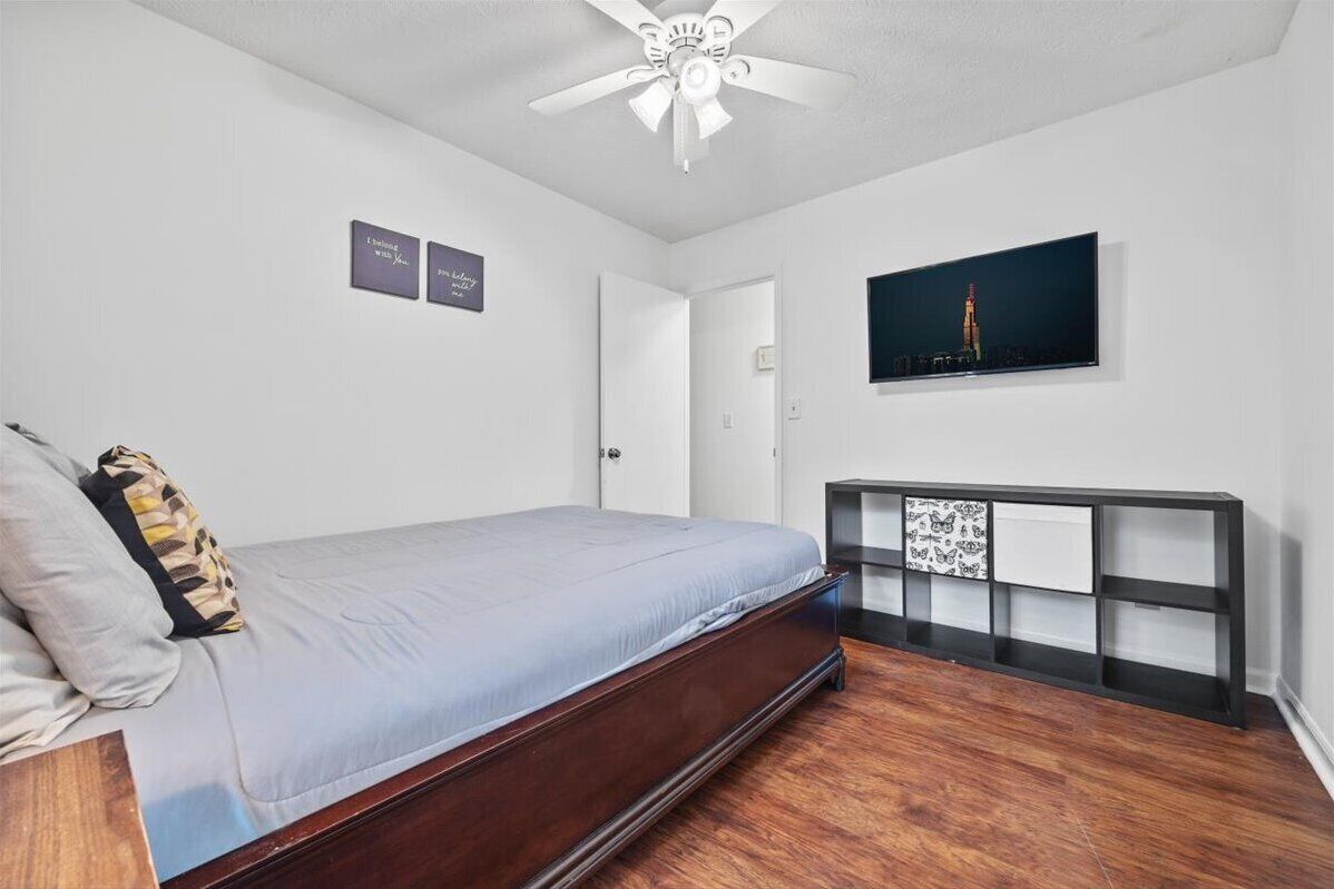 A bedroom with a bed, a ceiling fan, a wall-mounted TV, and a console table.