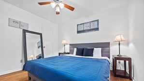 A bedroom with a bed, two bedside tables with lamps, a ceiling fan, a mirror, and wall art.