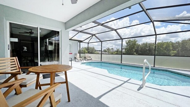 A pool area with a glass-enclosed structure, wooden furniture, and a clear view of the sky. - Sunny pool home with private deck - great location (Davenport)
