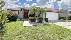 A single-story house with a red garage door, a front door, and a small front yard with trimmed bushes and a palm tree. - Sunny pool home with private deck - great location (Davenport)