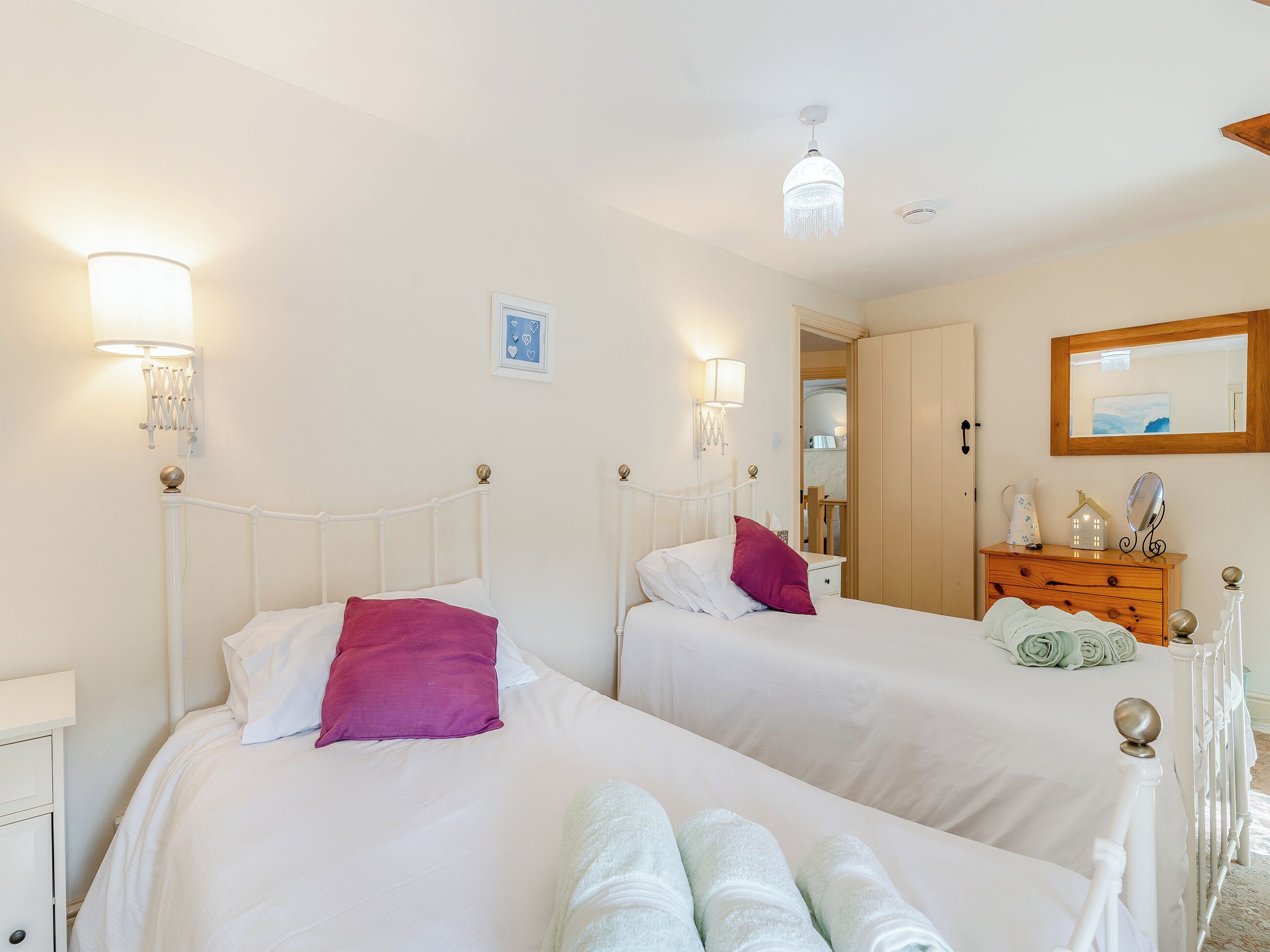 A hotel room with two beds, a wooden dresser, a mirror, and a chandelier.