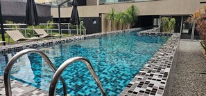 A swimming pool with tiled edges, lounge chairs, and umbrellas. - Elegance Suites Quatá (São Paulo)