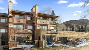 A modern multi-story house with a patio area, large windows, and a view of a hilly landscape. - Condo in Snowmass Village (Snowmass Village)