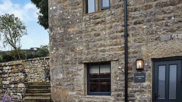 Un bâtiment en pierre avec une porte noire, une petite fenêtre et une enseigne sur laquelle on peut lire : « Balders Tunes Barn ».