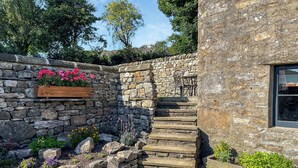 Un escalier en pierre mène à une porte en bois, qui est elle-même entourée d’un mur de pierre agrémenté de jardinières.