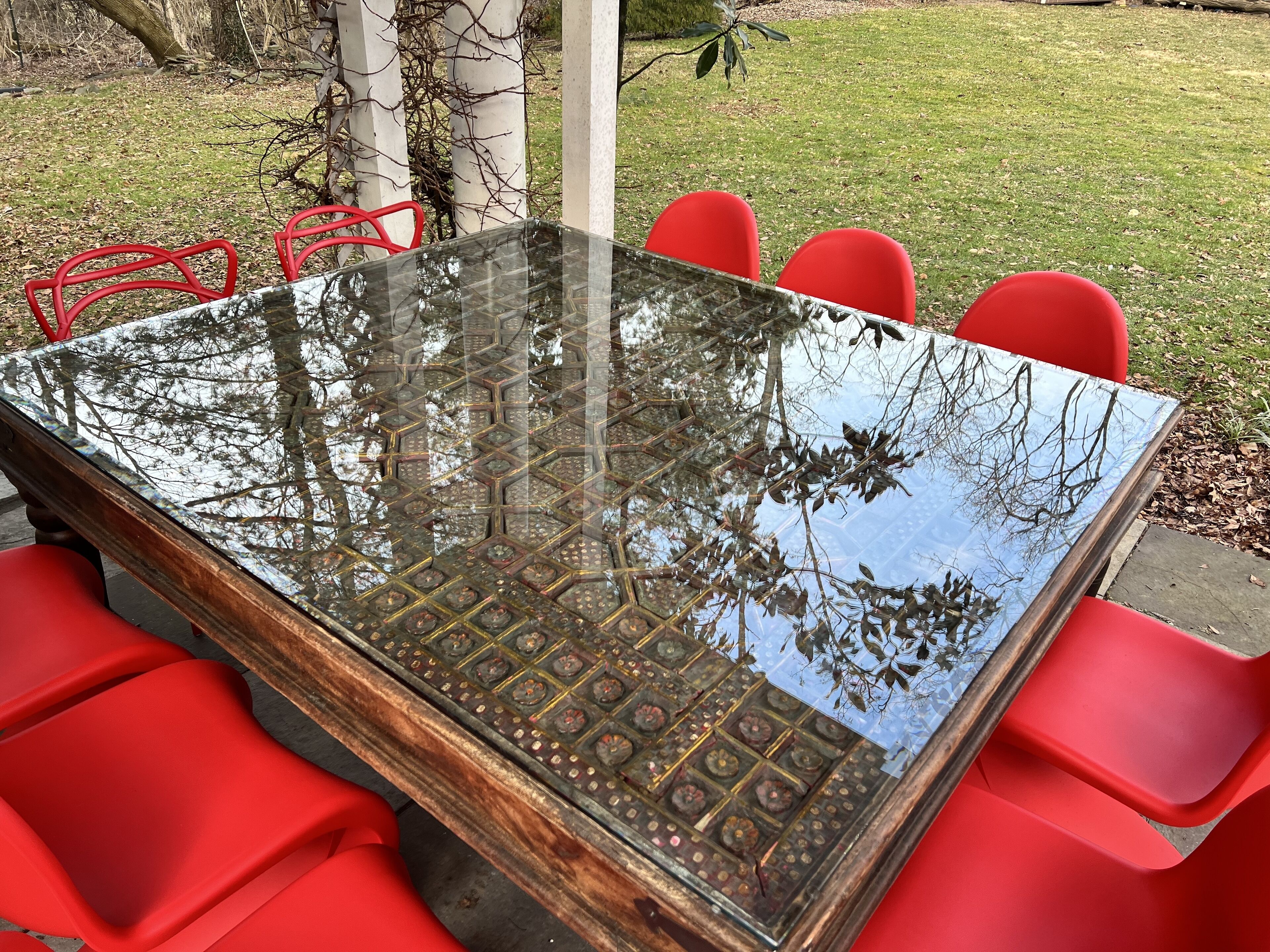 A glass-top table with a geometric pattern, surrounded by red chairs.