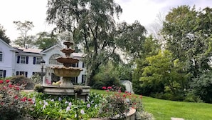 Ein Garten mit einer mehrstufigen Fontäne, umgeben von verschiedenen Blumen und Grünpflanzen.
