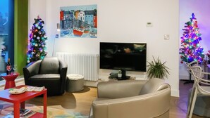 Un salon avec un canapé, un fauteuil, une télévision et un sapin de Noël.